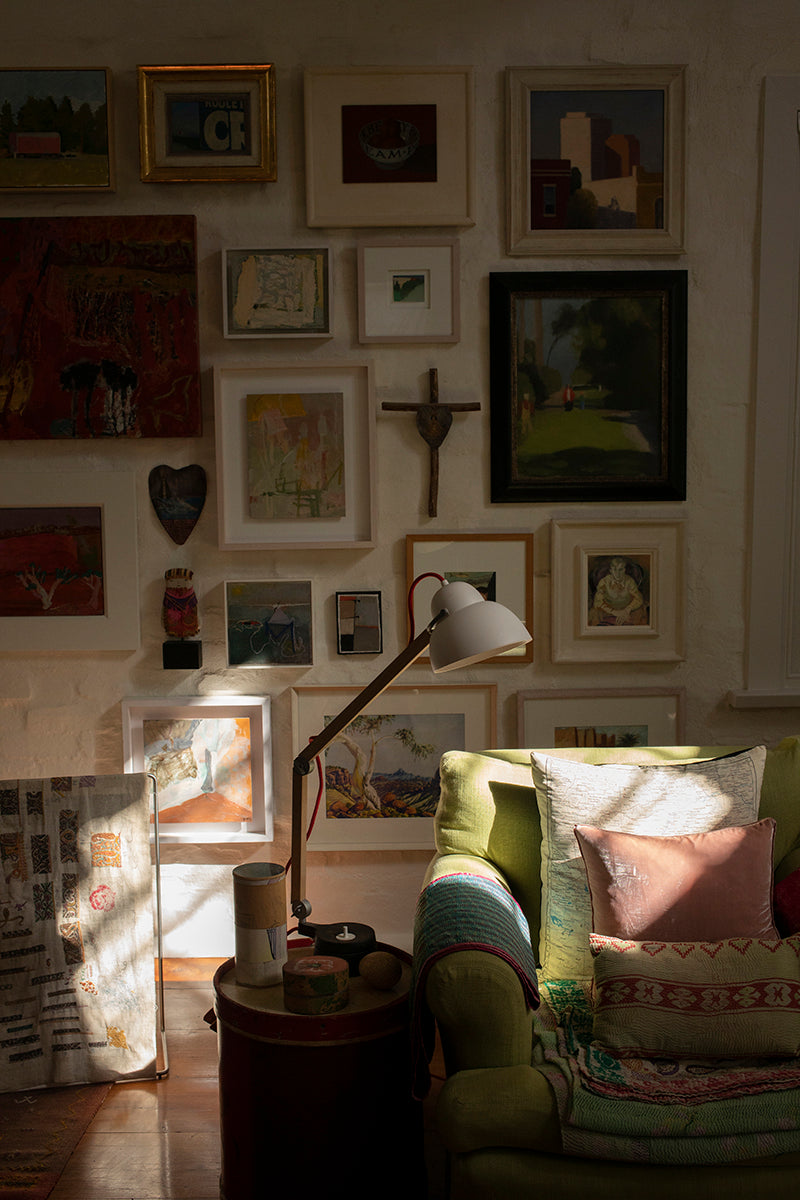 A picture gallery behind a comfortable green velvet sofa with pink cushions