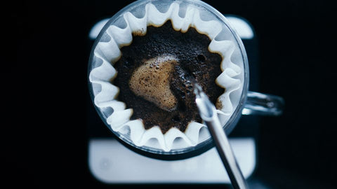 A person pouring hot water over a coffee filter filled with freshly ground coffee beans