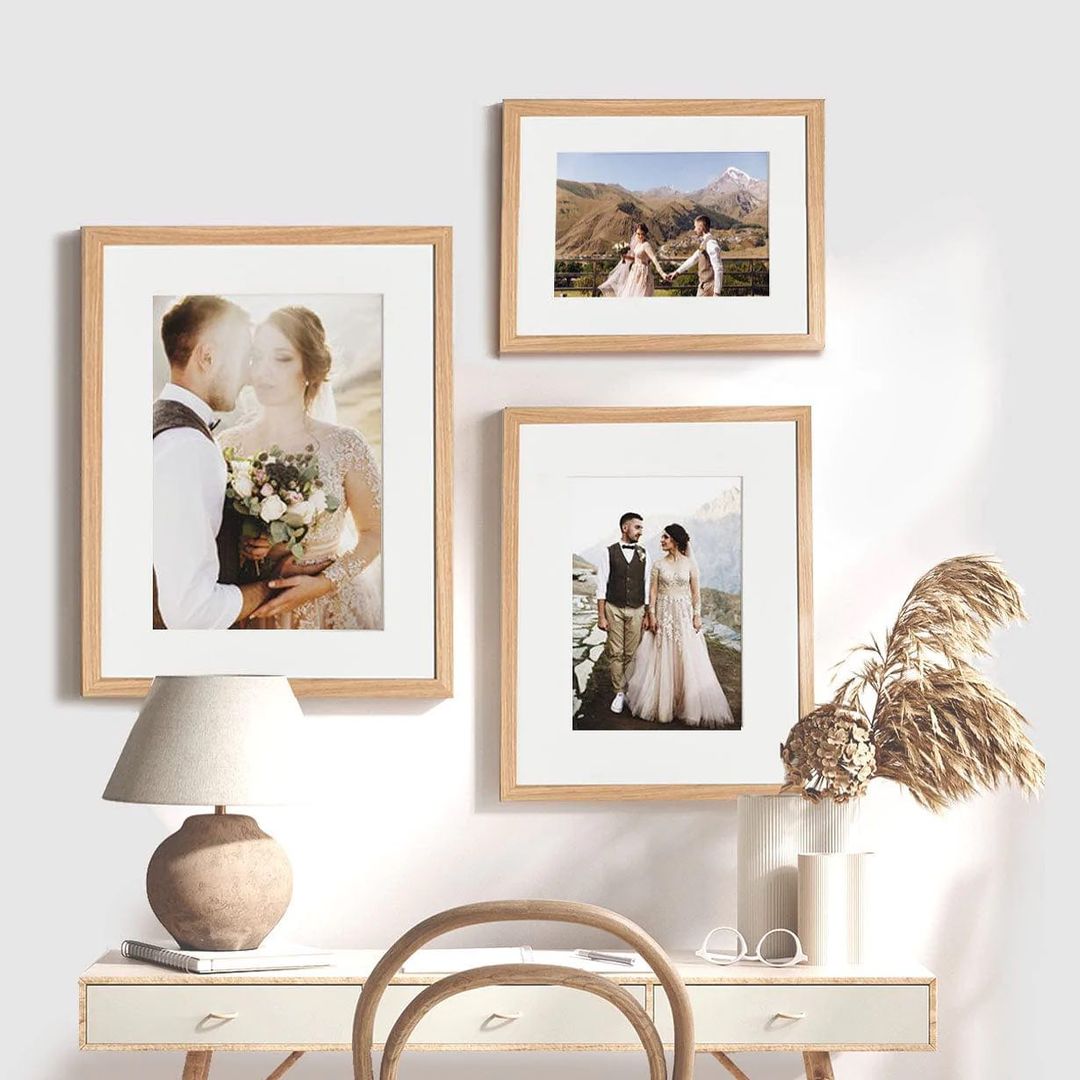Wedding photos in natural wood picture frames, displayed in a gallery wall above a desk with neutral decor.