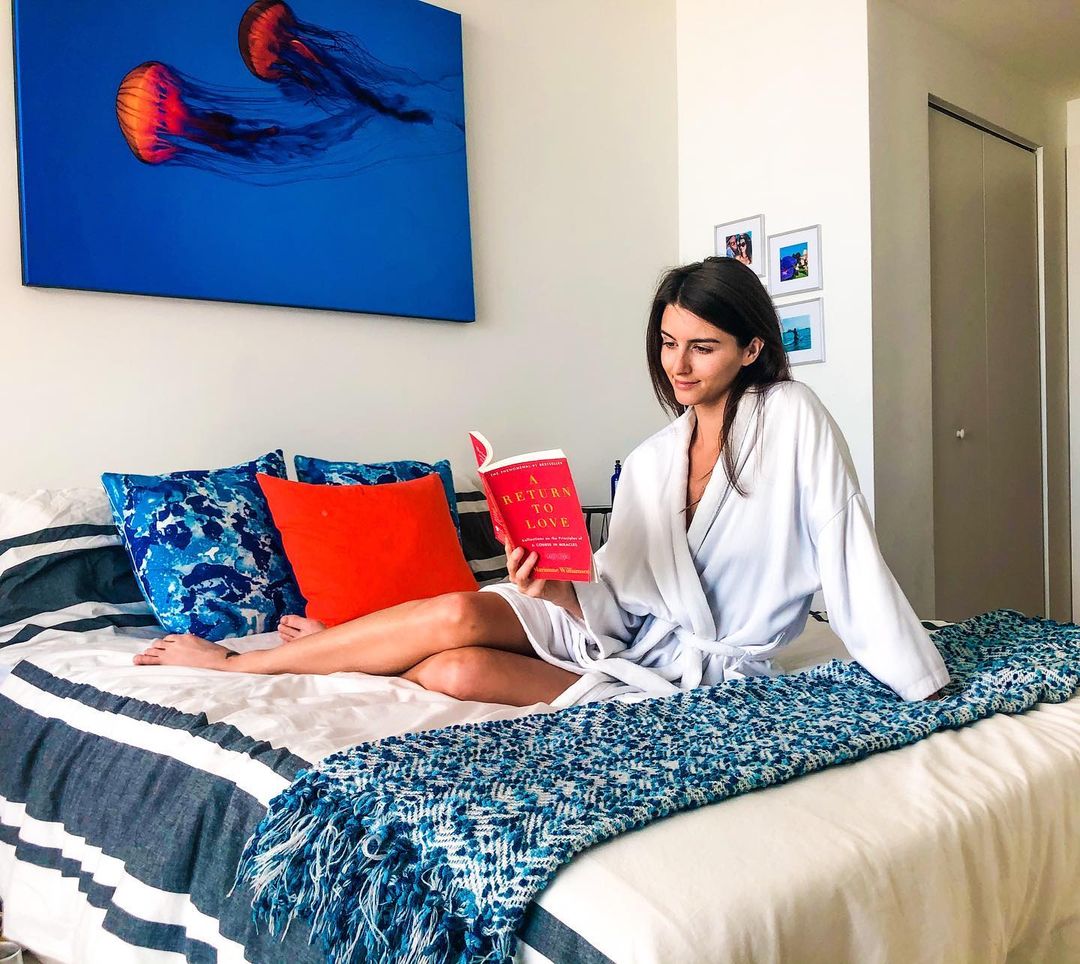 Woman reading in bedroom with large canvas print displayed on the wall above the bed.