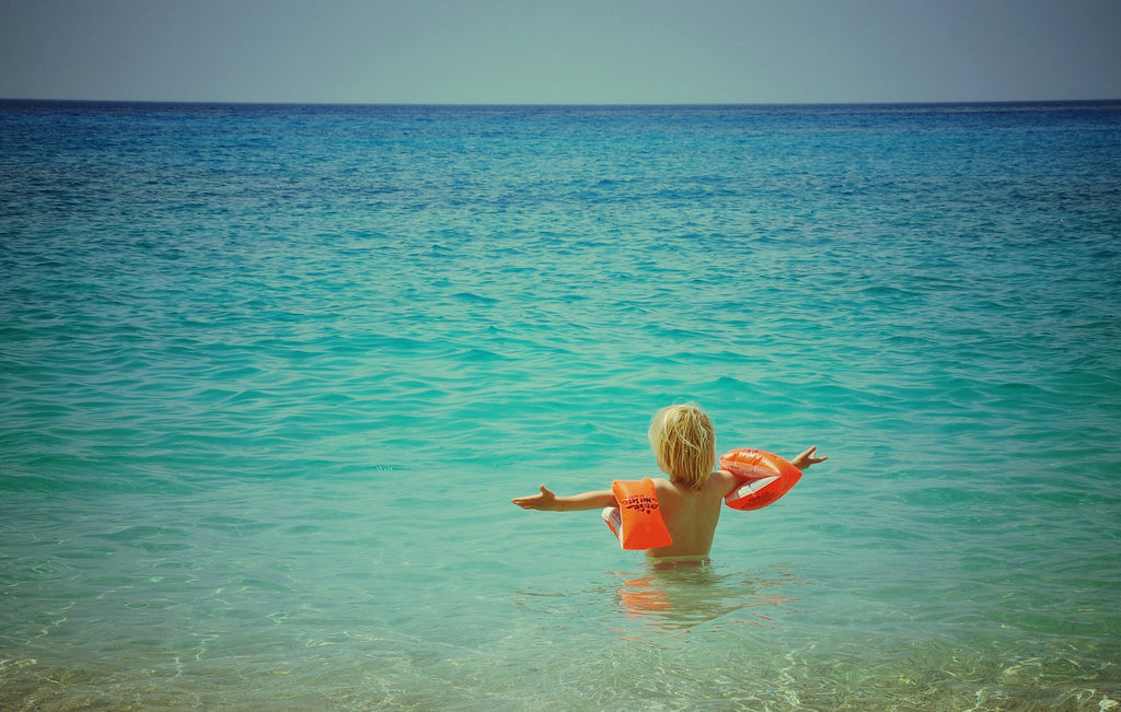 Beach photo of child in ocean wearing water wings