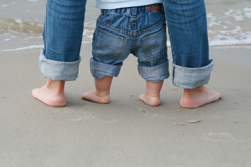 Close-up beach photo of adult and baby feet together in the sand