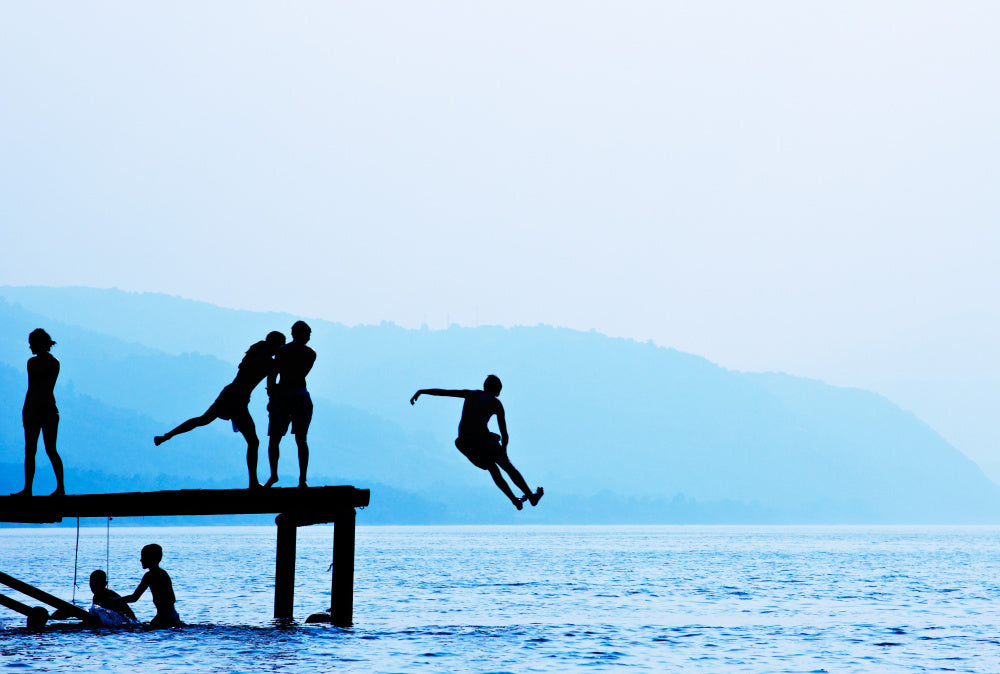 Silhouettes of a group of friends jumping off a dock into the water