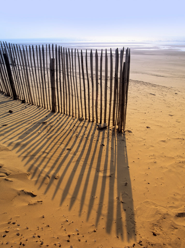 An old wooden fence and its shadows on a sandy beach