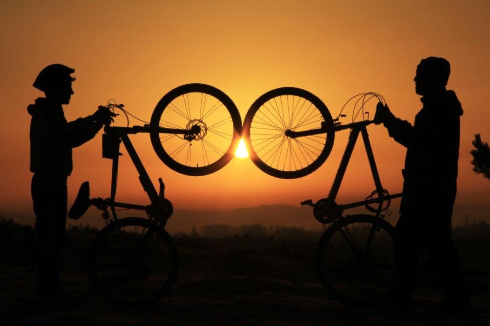 Sunset silhouette of two people holding up their mountain bikes