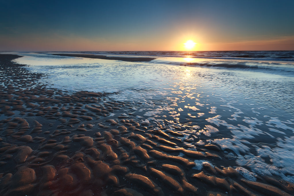 Ocean landscape photo at sunrise or sunset with wet ripples in sand