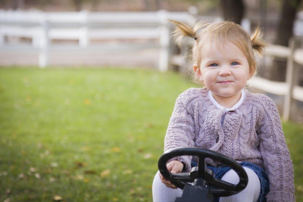 Cute little girl in pigtails sitting on a toy outside - example of the rule of thirds in photography