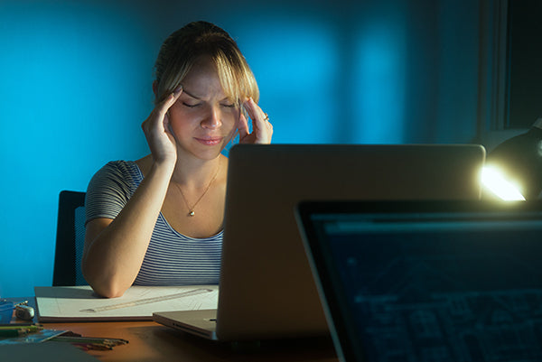 Woman at computer with headache caused by not wearing proper computer glasses