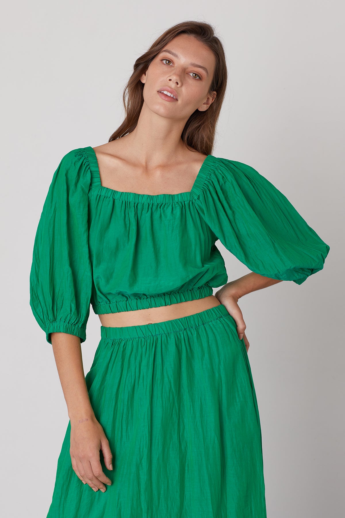 Model standing with one hand on hip wearing Bristol puff sleeve crop top in bright emerald green and Mariela skirt