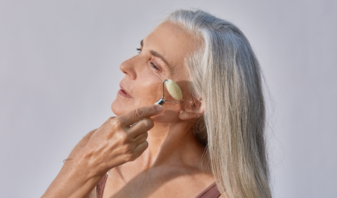 Woman with silver hair using jade roller tool on cheekbone
