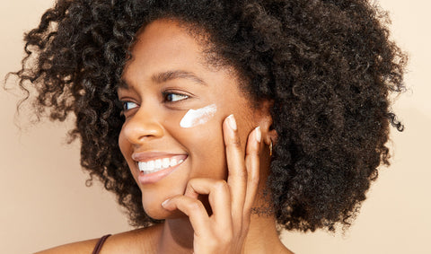Woman applying moisturizer to her cheekbone.