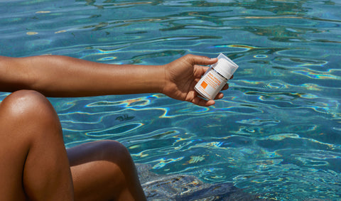 Model holding sunscreen against backdrop of clear blue water