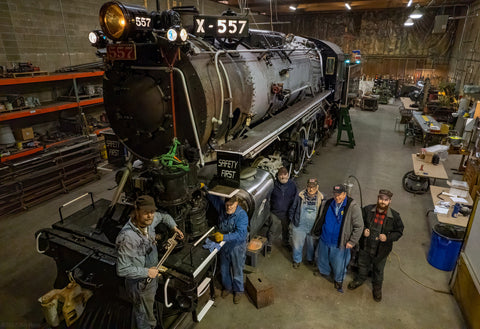 Volunteers in shop gather for picture beside the restoration project of Alaska's Engine 557