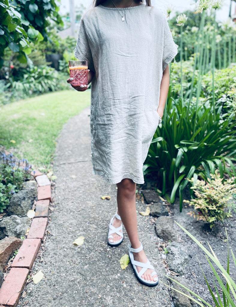 Woman walking through garden wearing the Eadie Lifestyle Pocket Linen Dress in natural