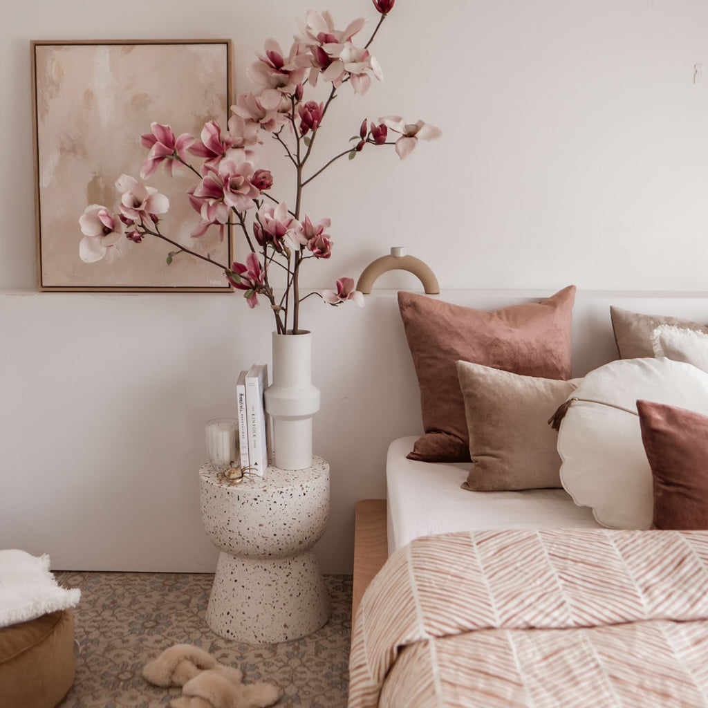 Spring bedroom with layered velvet cushions, stone terrazzo stool and Magnolia flowers