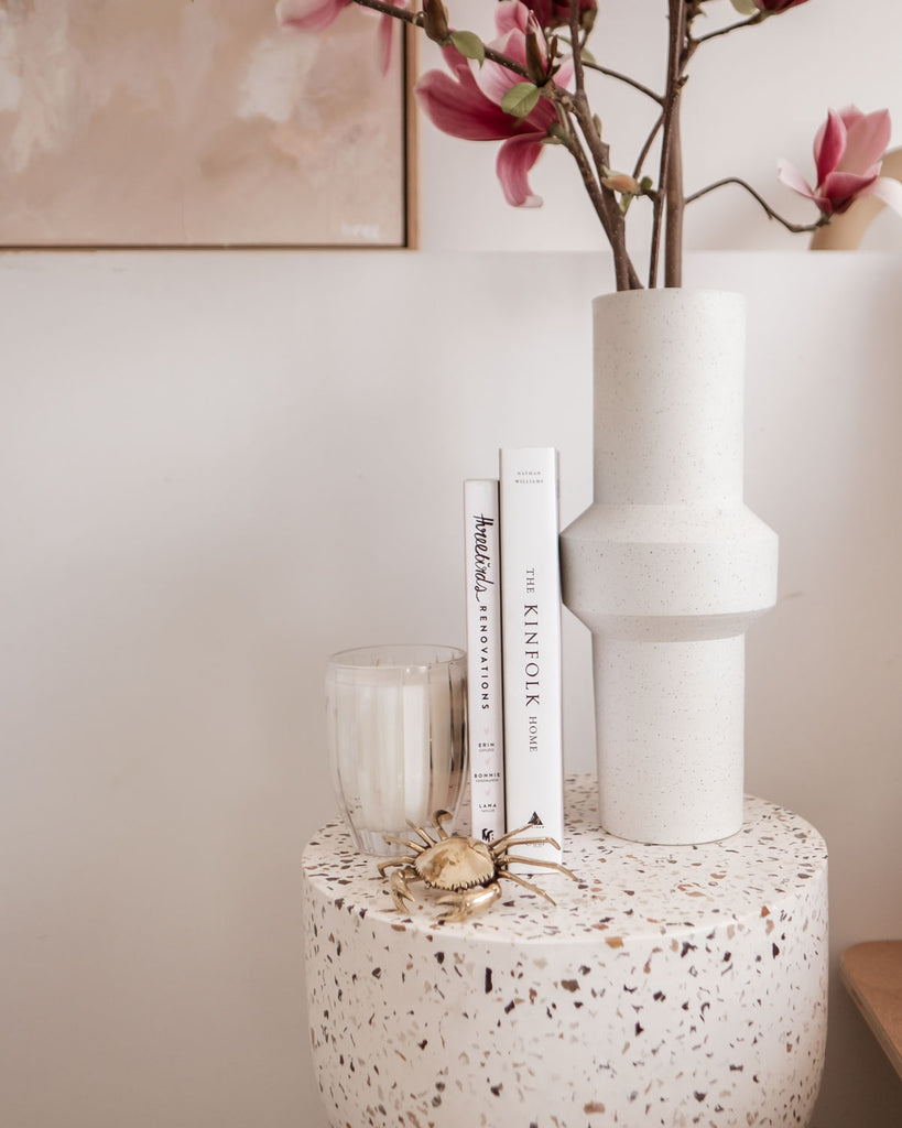 Some books and a vase filled with magnolias sit atop the terrazzo side table