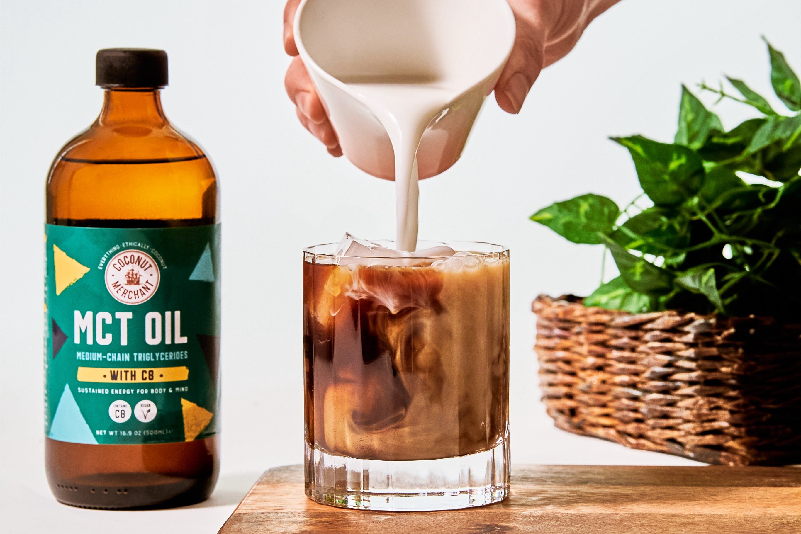 Bottle of MCT oil with someone pouring in coconut milk into a small glass of coffee next to it