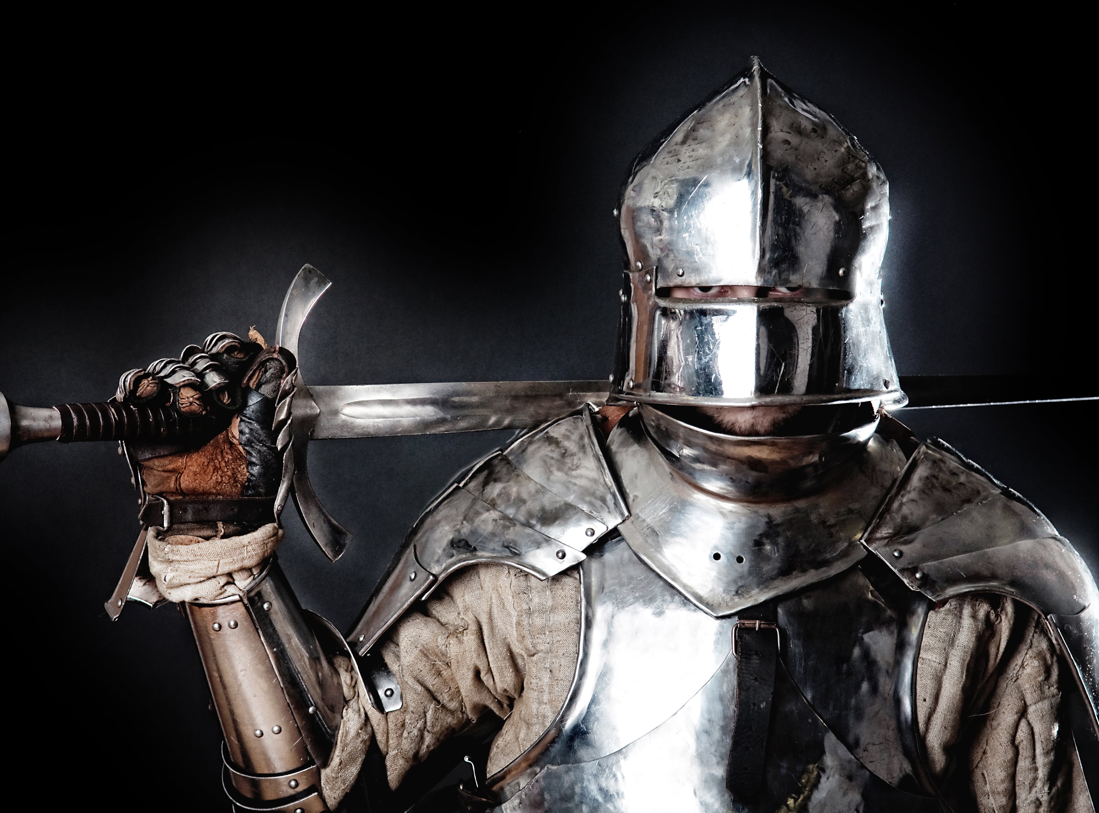 A soldier wearing metal armor and a metal helmet holding a steel sword resting on his back.