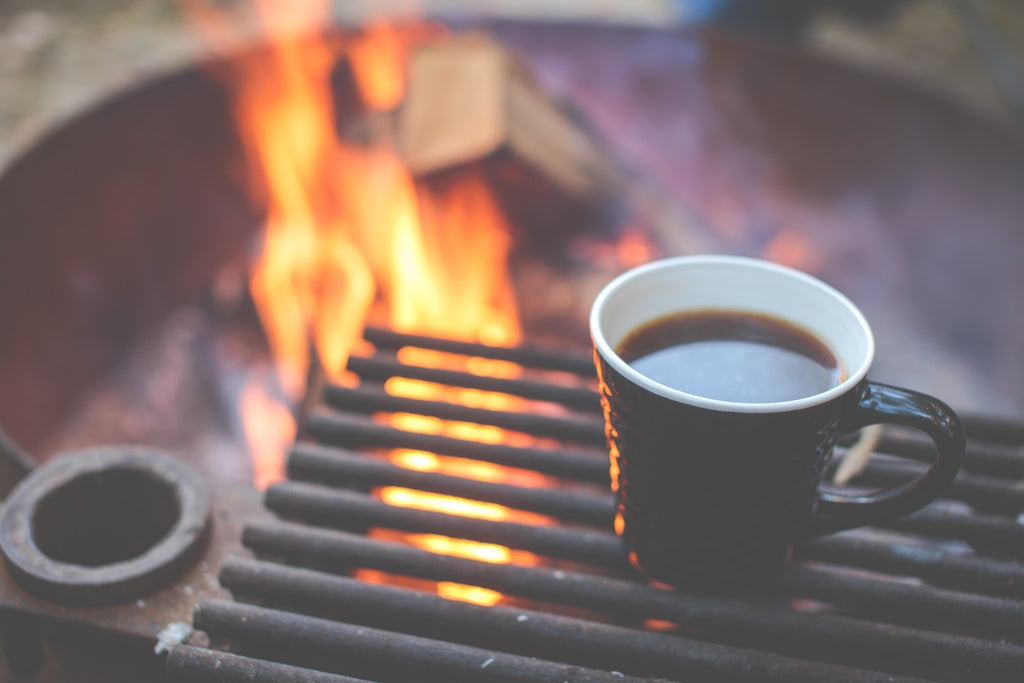 Cup of black coffee warming next to a campfire. Photo by Alex Holt on Unsplash