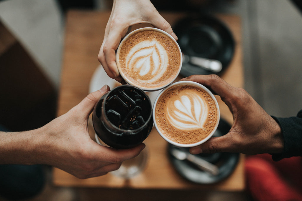 Three friends with lattes and iced coffee clink glasses in a toast. Photo by Nathan Dumlao on Unsplash