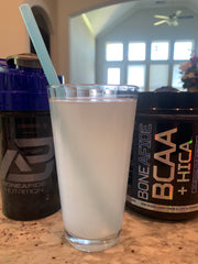 a glass of BCAA+HICA mixed with water stands on a counter in front of the product jar and a sports drink container