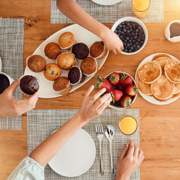 Hands reaching for delicious breakfast items including muffins and pancakes