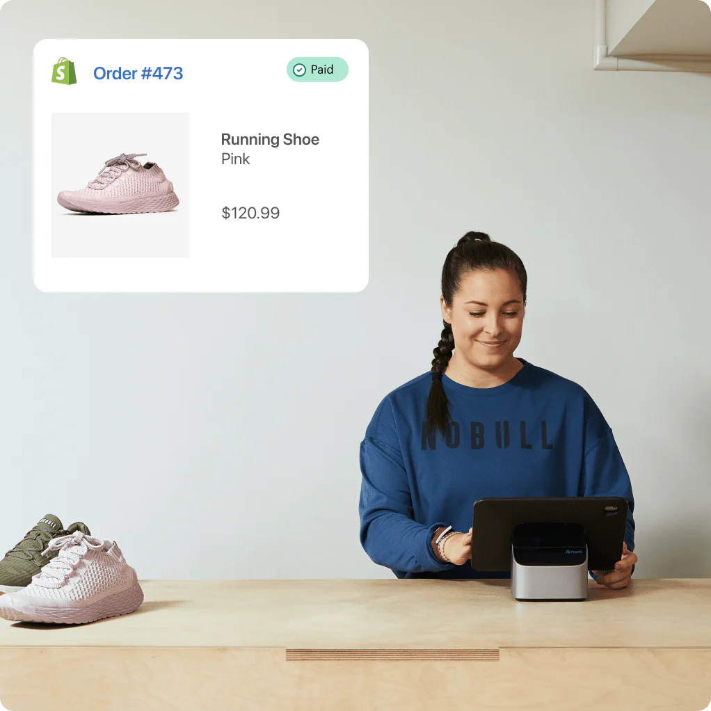 A smiling woman sits at a counter, smiling at a tablet device in front of her. There are two shoes to the left of her, and in the upper left, an order paid confirmation screen with a shoe, a description of “Running shoe - pink” and a cost of ₹9,797.78.